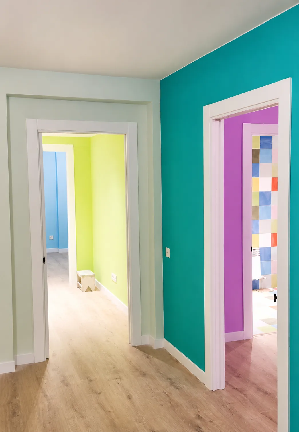 Pasillo con paredes pintadas en turquesa, verde lima y magenta, y baño con azulejo de colores al fondo