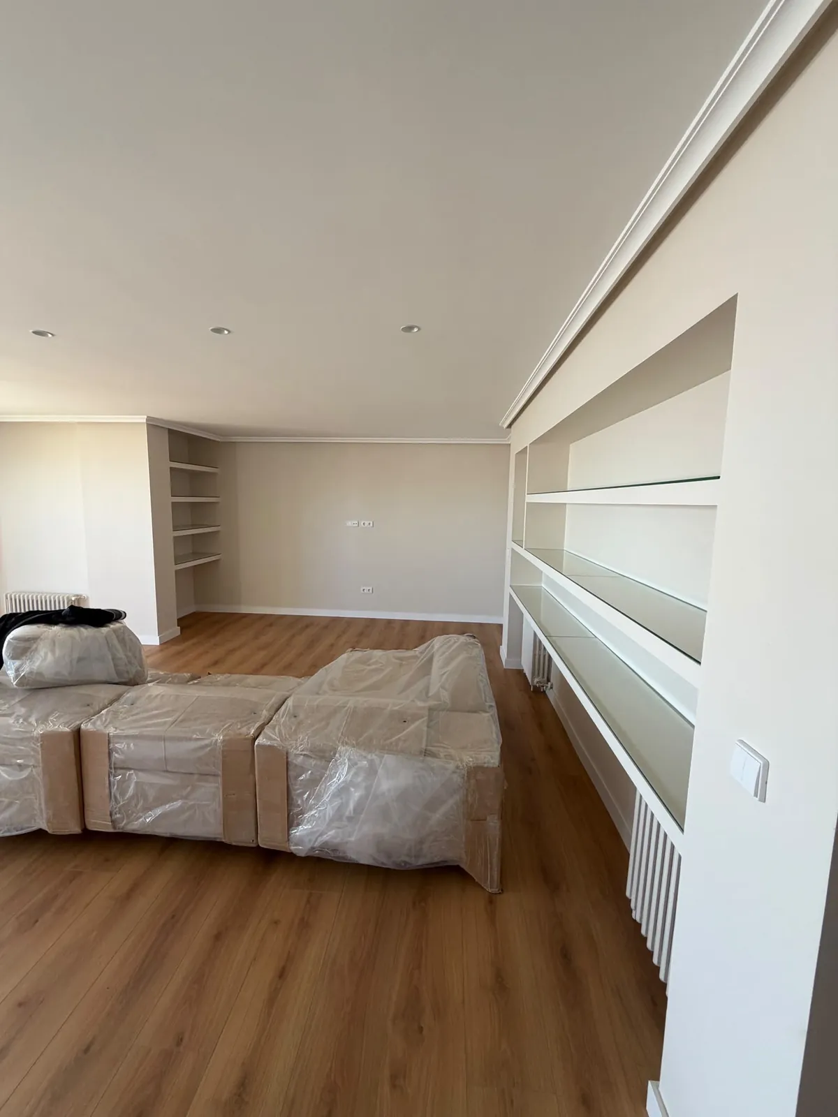 Salón con librería a medida en blanco, estantes de cristal y suelo de madera