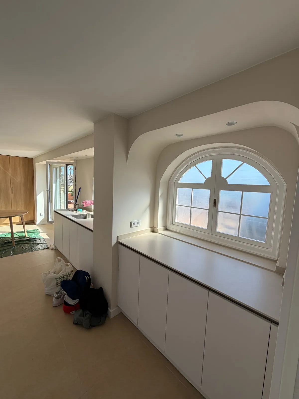 Cocina abierta con ventana en arco, mobiliario en madera clara y luz natural