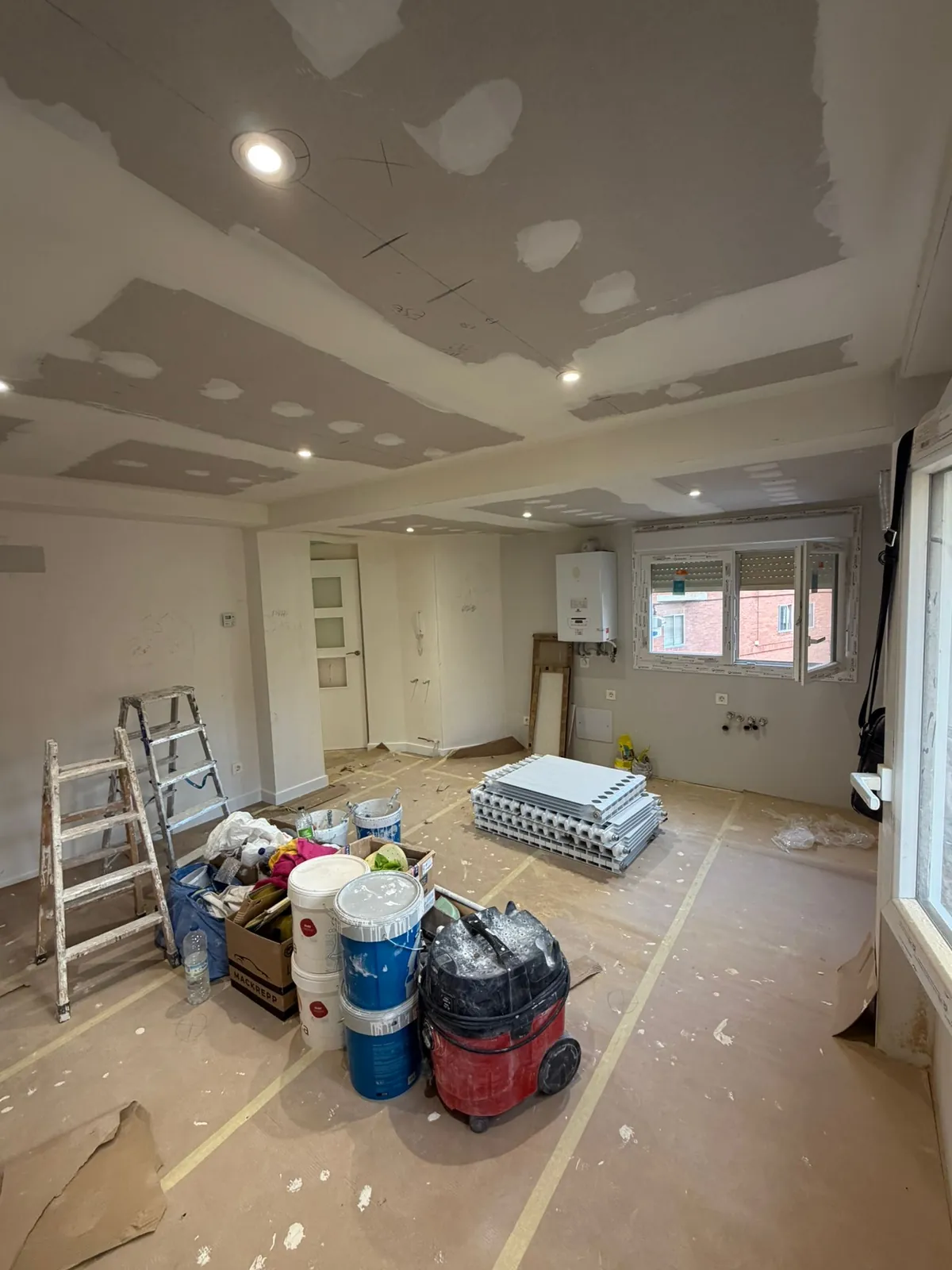 Escalera, botes de pintura y aspirador de obra en una habitación en plena ejecución
