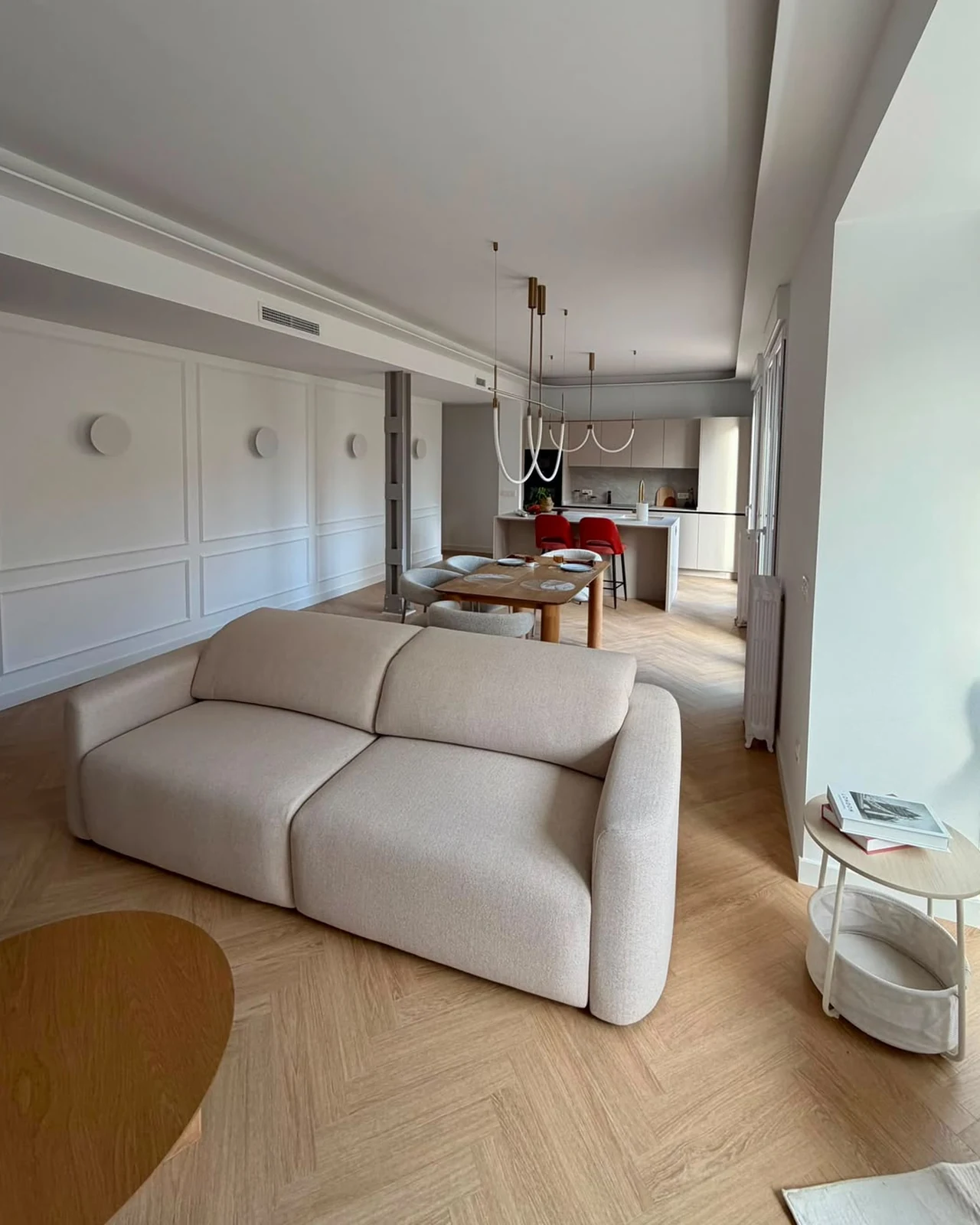 Salón de una vivienda de Zaragoza con pared de molduras pintada en blanco, techo liso y paso al comedor y la cocina