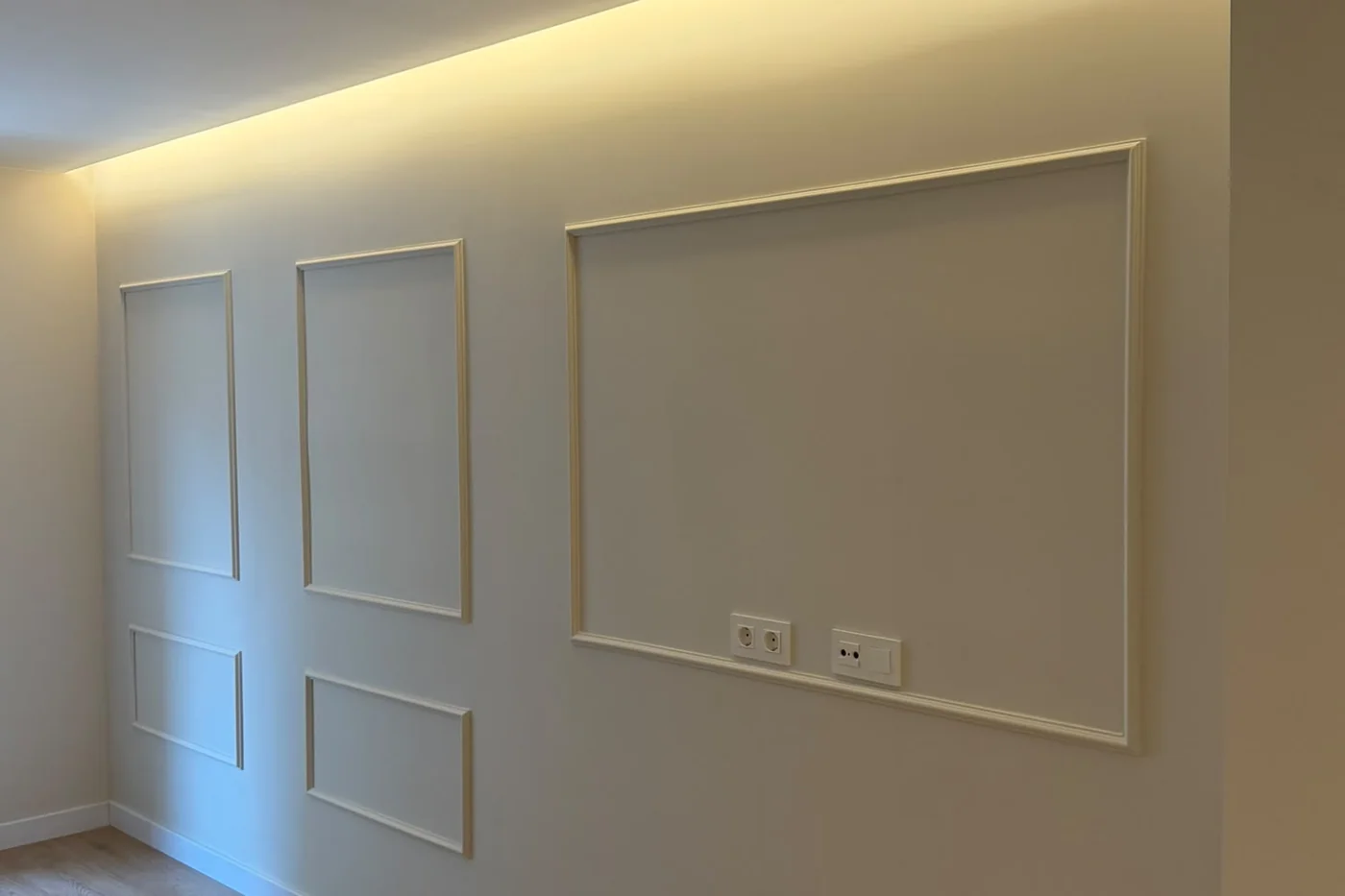 Pared con molduras y plafones pintados en blanco, con luz indirecta