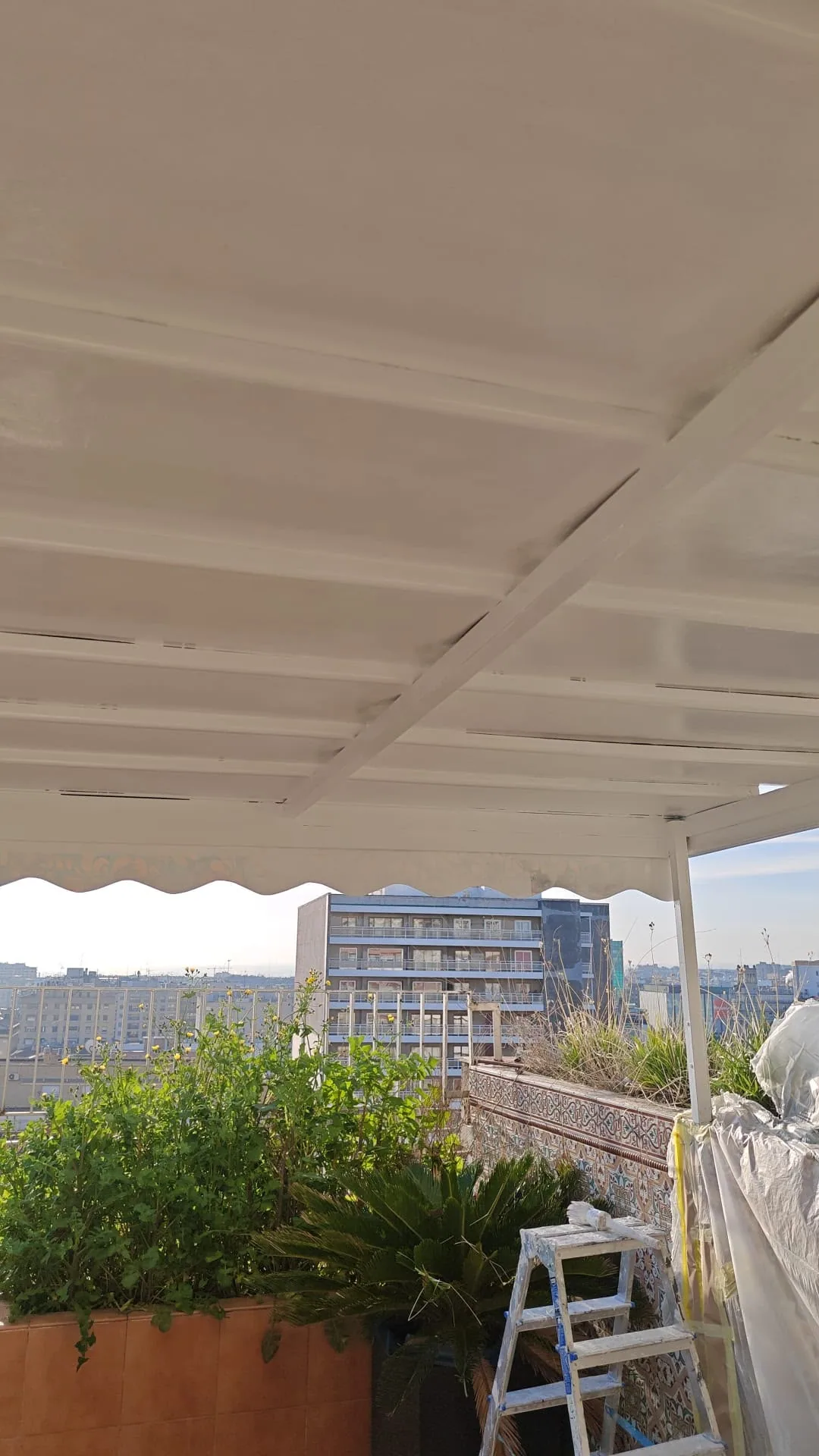 Pérgola metálica de una terraza esmaltada en blanco, con el toldo recogido